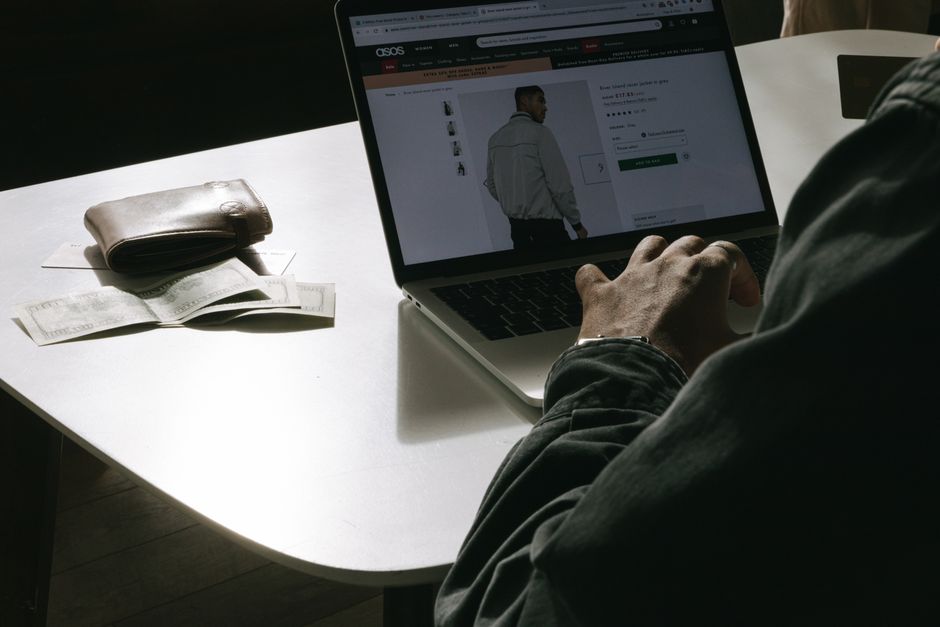 google shopping setup — Adult man shopping for clothes online at home using a laptop, with a wallet on the table.