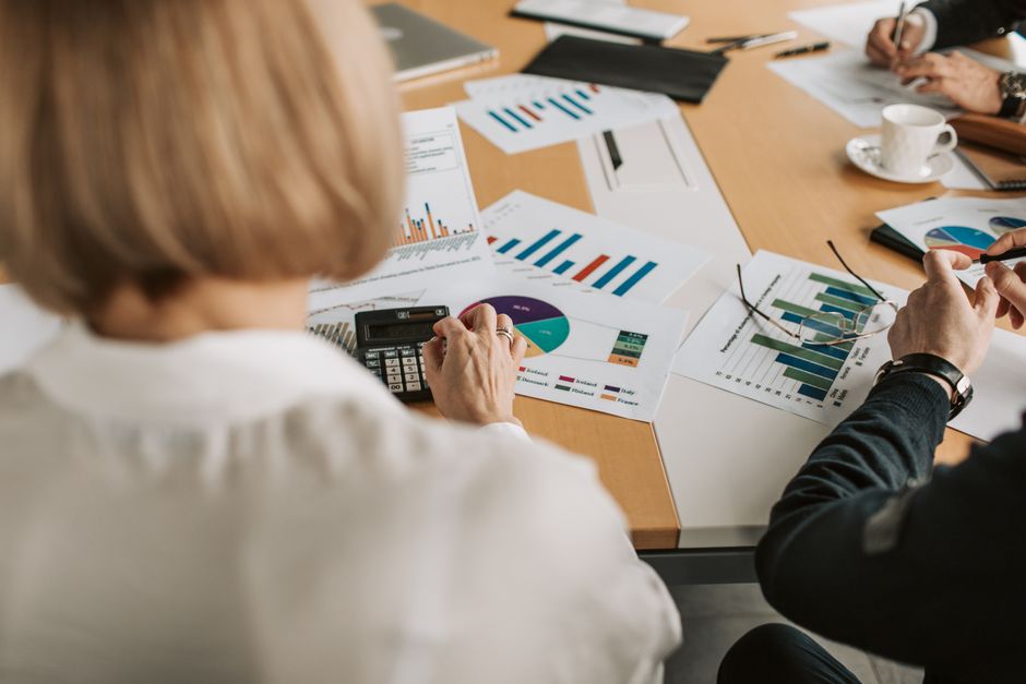 roi marketing agency — Overhead view of professionals discussing financial graphs and using calculators in an office set