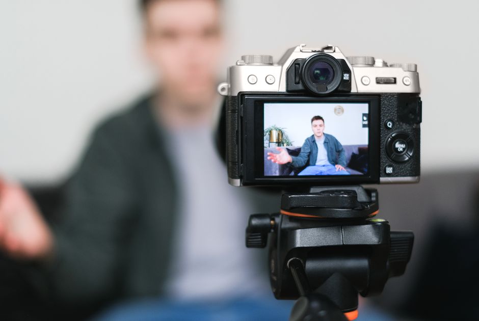 influencer marketing ไทย — Man recording a vlog indoors using a mirrorless camera on a tripod with selective focus.