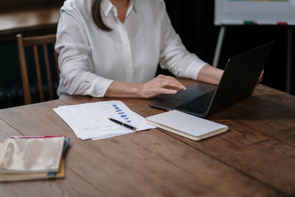 keyword research b2b — Businesswoman in white shirt working on laptop with papers at wooden desk.