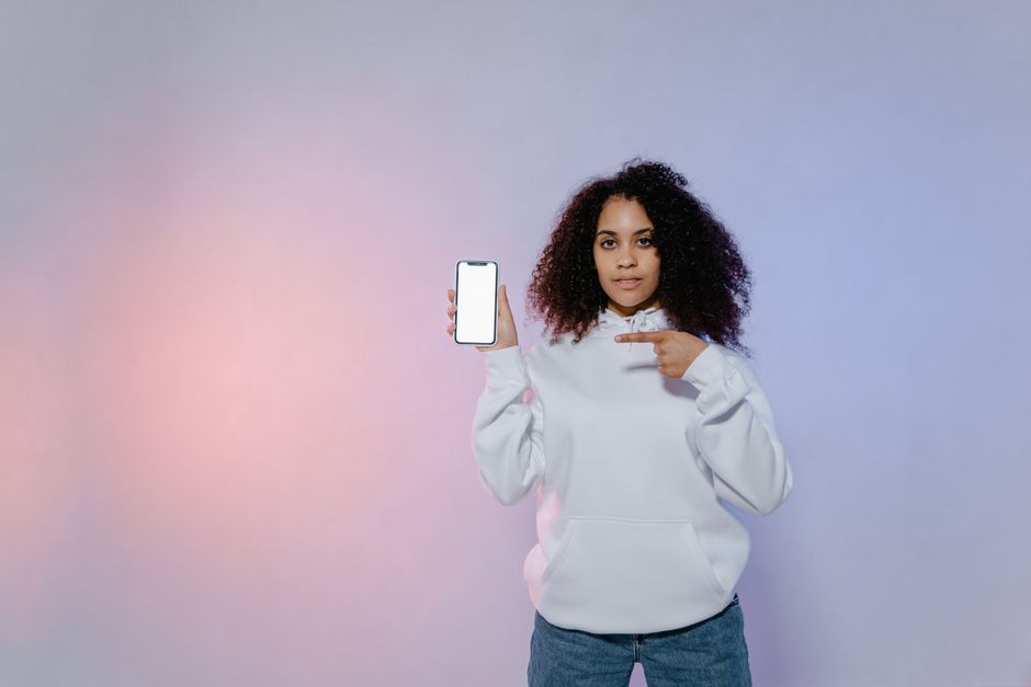 line marketplace ads — Woman in white hoodie pointing at a smartphone with blank screen, ideal for mockup designs.