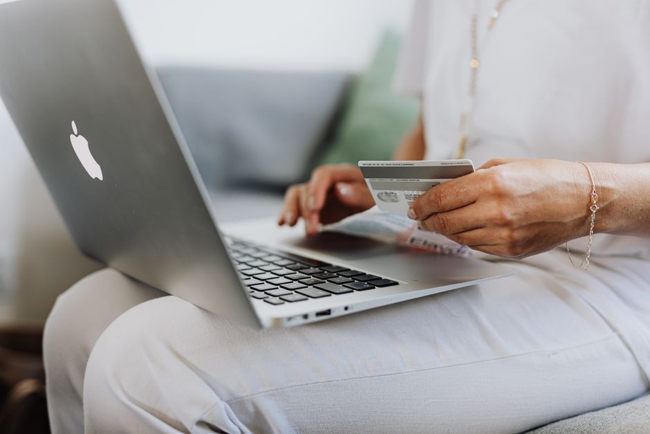 meta ads ขายของ — Close-up of a person holding a credit card while shopping online using a laptop at home.