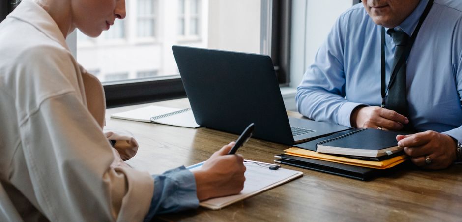 คำถาม agency โฆษณา — Crop faceless colleagues in formal clothes sitting at table with laptop and folder and signing docu