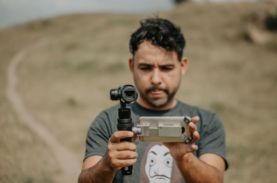 tiktok ads วิดีโอ — Man using a smartphone gimbal for videography on a grassy field.