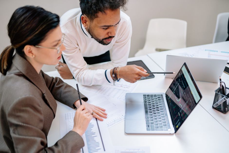 cro b2b — Business professionals discussing data at a desk with a laptop.