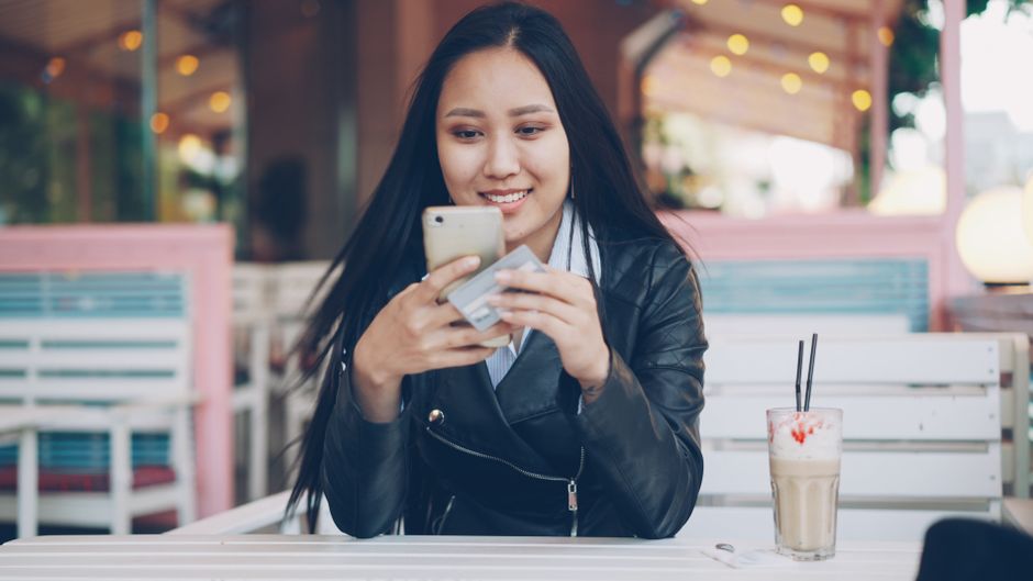 customer journey b2c — Smiling woman at café using smartphone and credit card for online shopping.