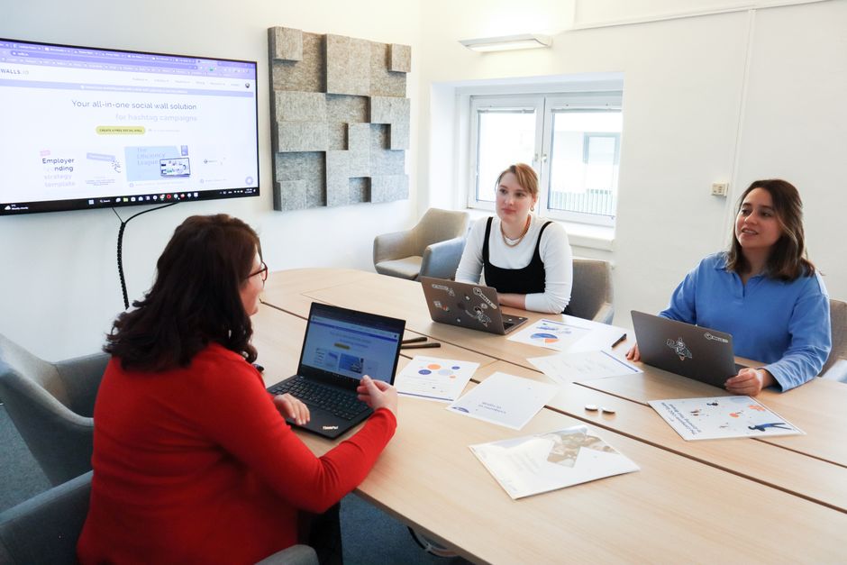 email segmentation — Three women collaborating at a conference table in a modern office with laptops and presentation sc