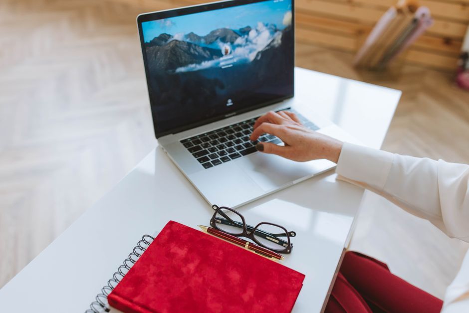 form optimization — A person working on a laptop with a red notebook and glasses on a white table.