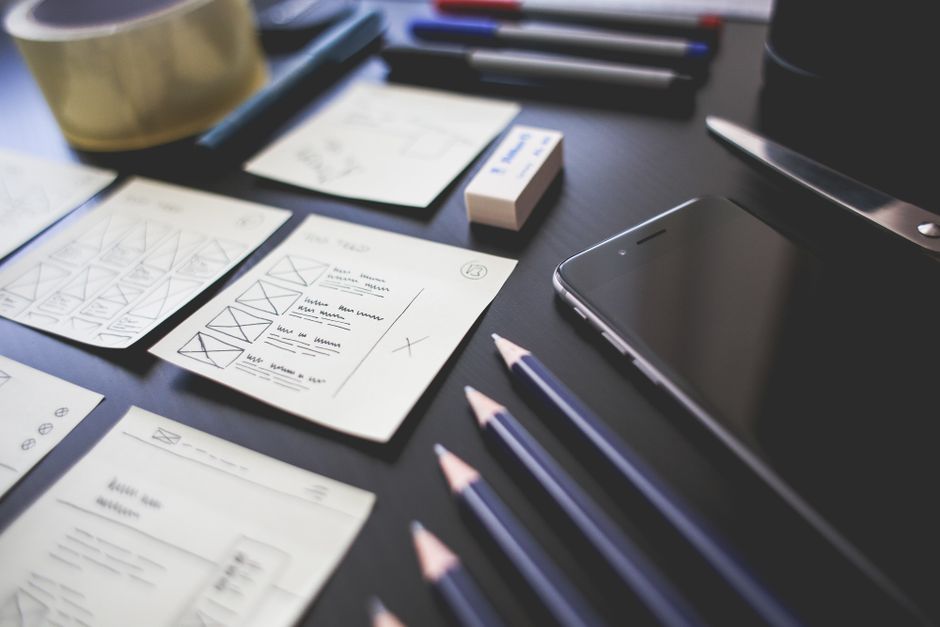 landing page conversion — A creative workspace featuring UI design plans, pencils, a smartphone, and other office tools.