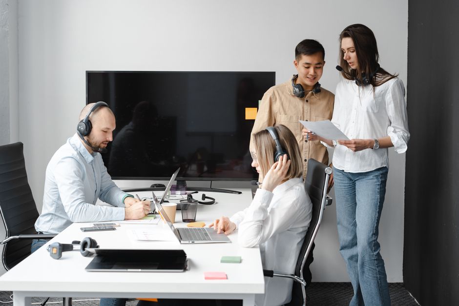 lifecycle marketing — A diverse group of coworkers collaborating in a modern office space with headsets and laptops.