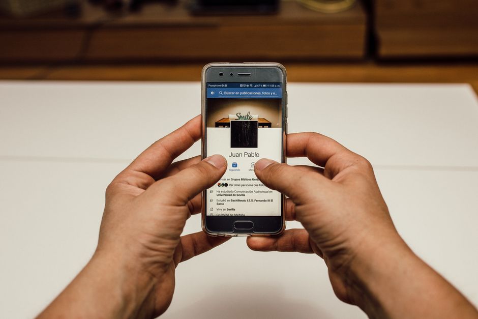 line oa community building — Close-up of hands using a smartphone with a social media page indoors.