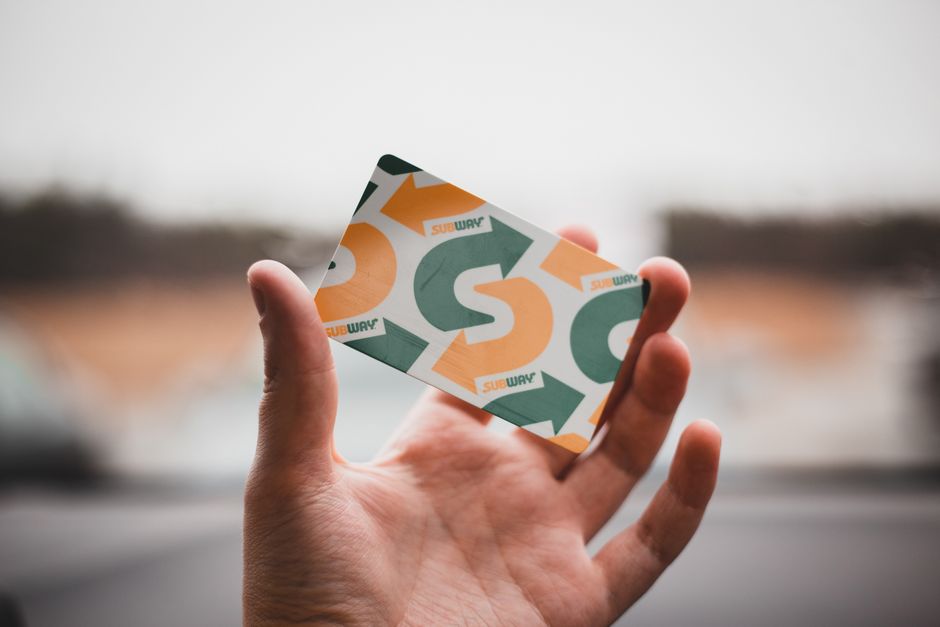 loyalty program ไทย — A hand holding a colorful gift card with arrows and text against a blurred background.