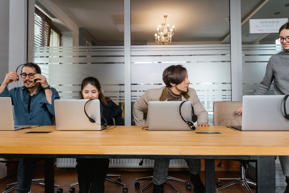 จัดการรีวิว — Business professionals working in an office with laptops and headsets, engaging in teamwork.