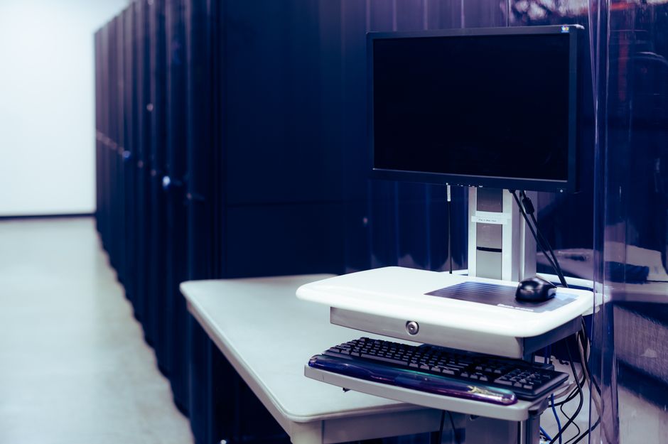 server side tracking — Contemporary computer with black screen placed on stand near row of server steel racks in data ce