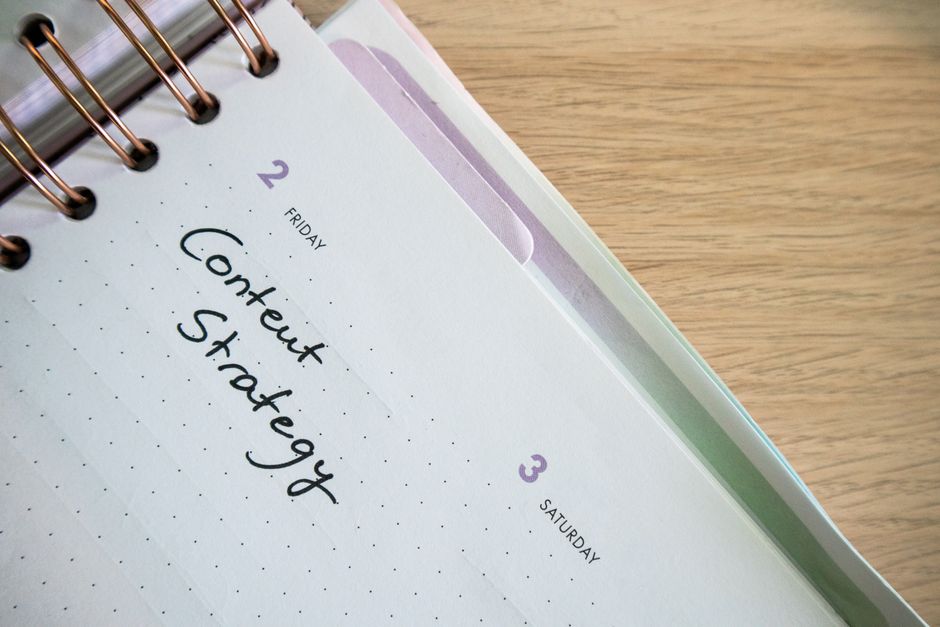 topical authority — Top view of a notebook open to a day planner featuring 'Content Strategy' handwritten, lying on a wo