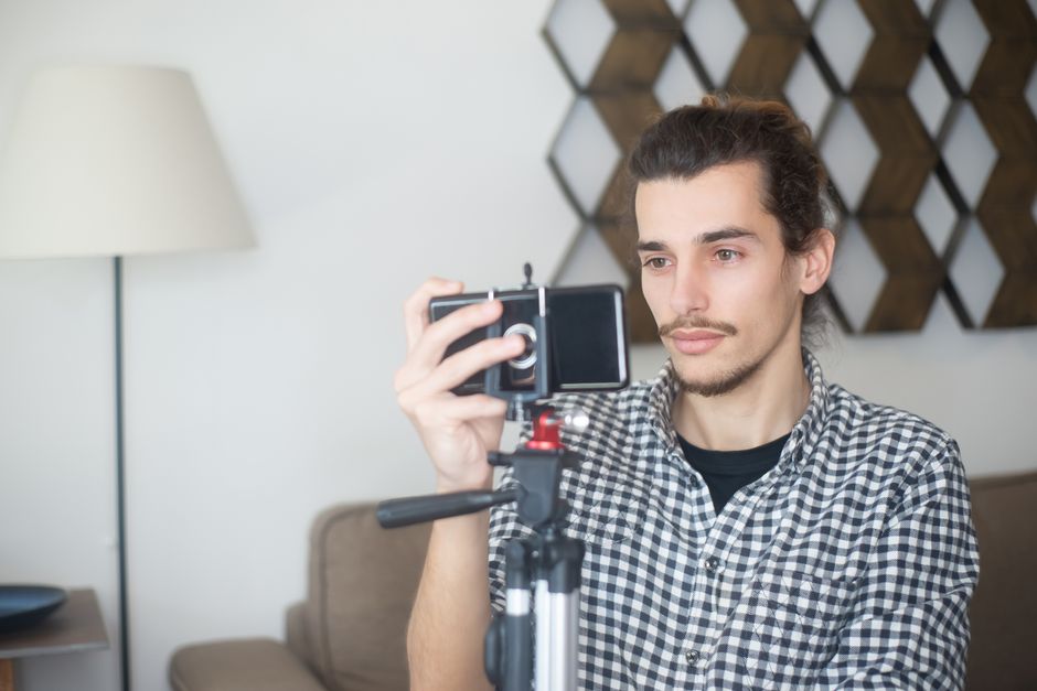 ugc คือ — Young man with plaid shirt using a smartphone and tripod to create content indoors in Portugal.