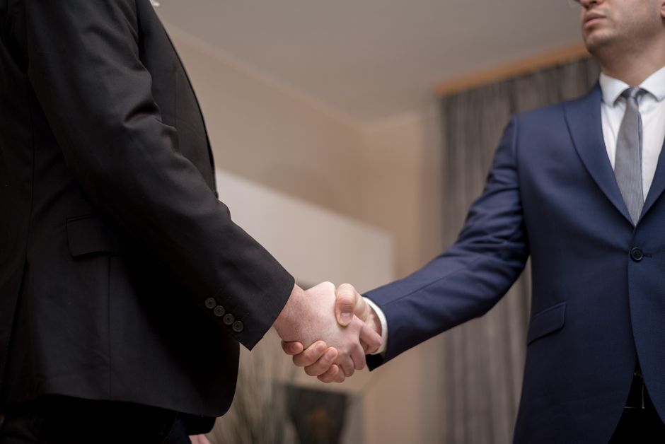 b2b affiliate — Two businessmen in suits shaking hands, emphasizing trust and partnership indoors.