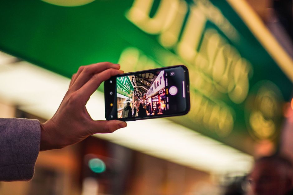 facebook reels ads — A person takes a vibrant city street photo with a smartphone at night, showcasing technology's role