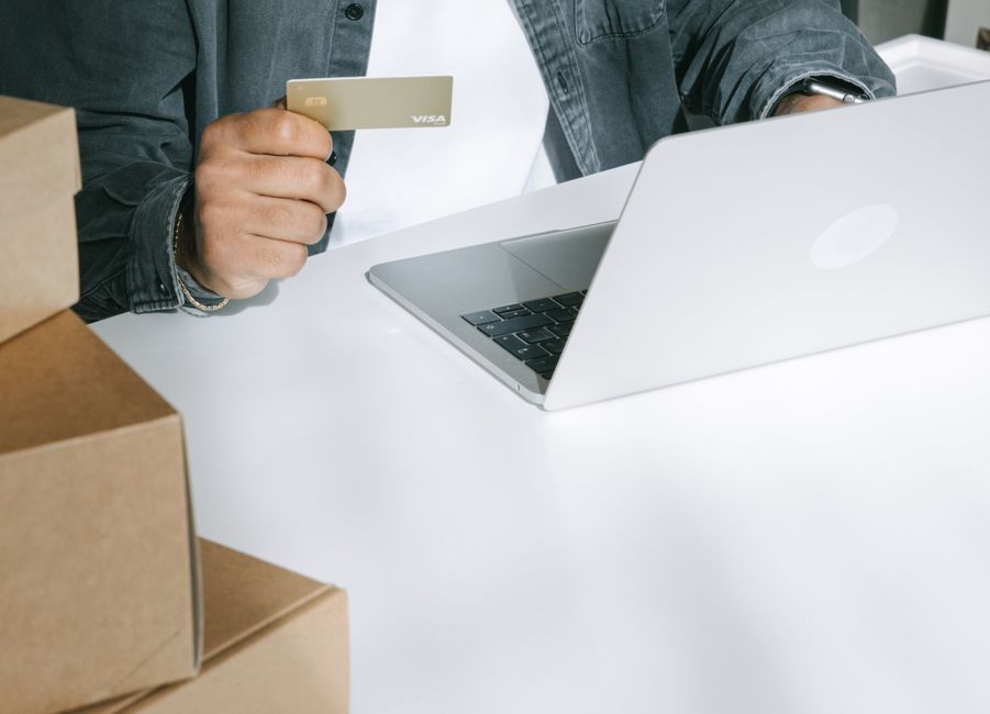 product feed optimization — Person using a credit card for online shopping on a laptop surrounded by shipping boxes.