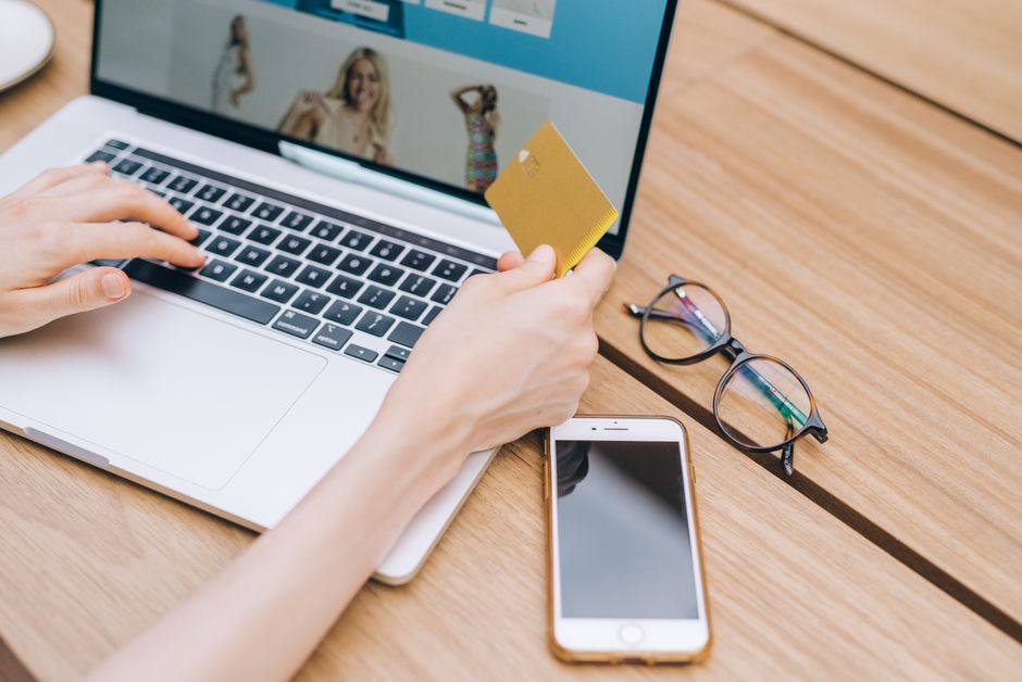 shopee ads ตั้งค่า — A person makes an online purchase using a credit card on a laptop, with a smartphone and glasses ne