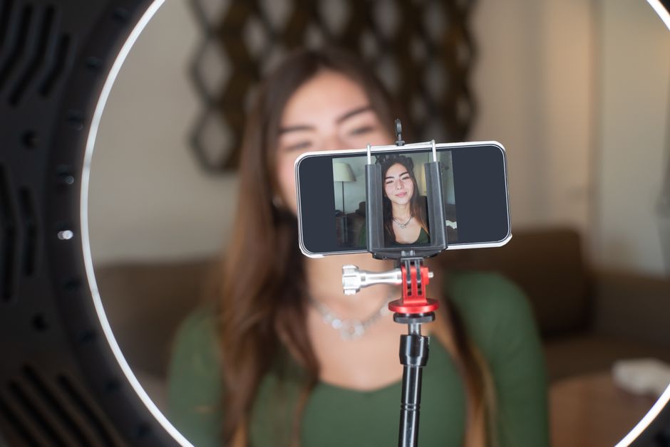 shopee live — A young woman live streams from home using a smartphone and ring light setup.
