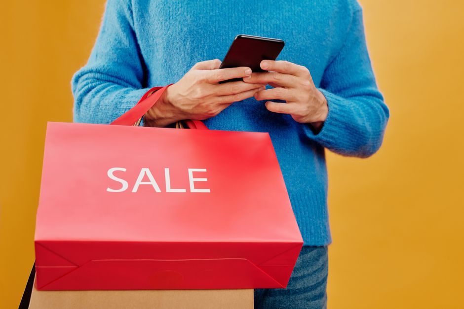 social proof — Close-up of a man holding a sale bag and smartphone, symbolizing shopping and discounts.