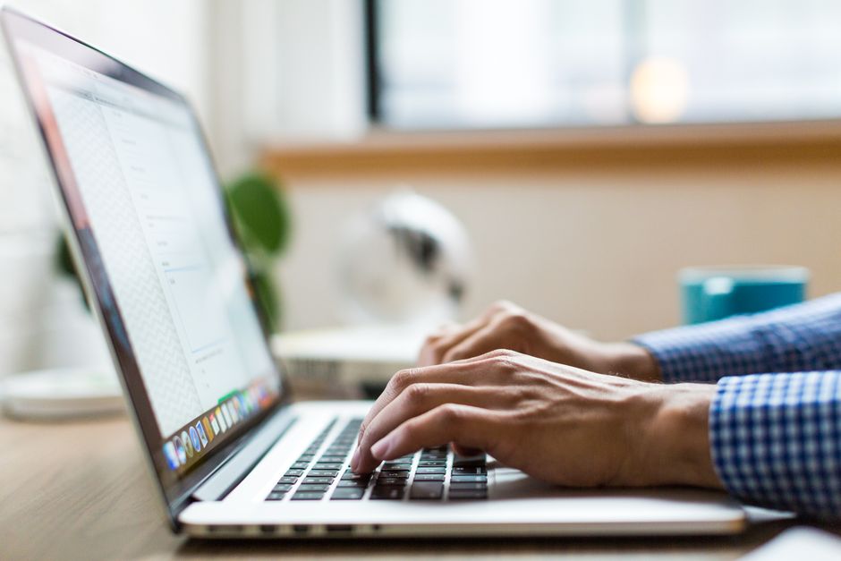 welcome email — Close-up of adult typing on laptop in bright, modern office.